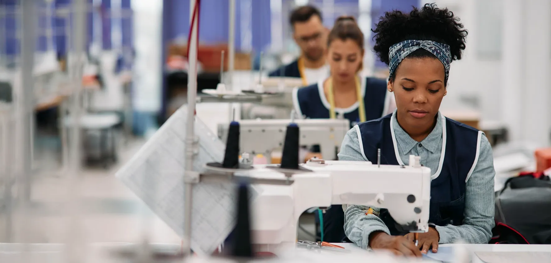 People working at sewing machines in a garment factory, focusing on their tasks.