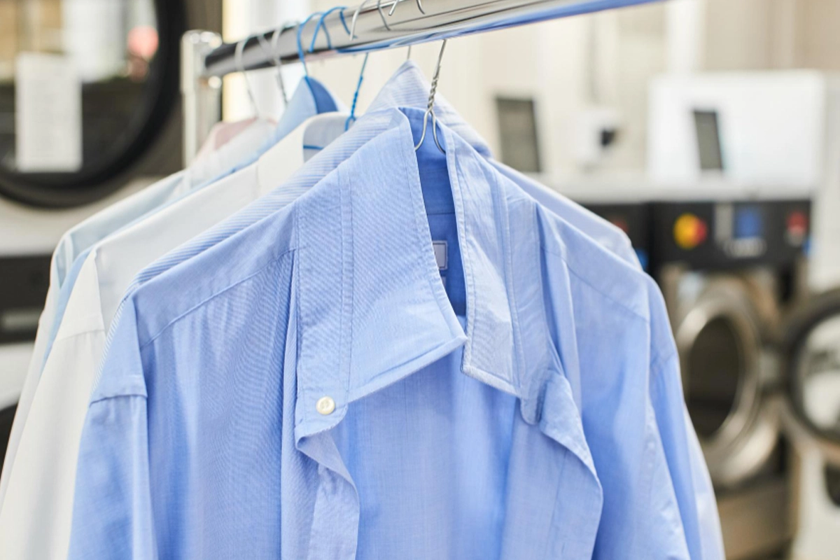 Several freshly-laundered dress shirts, including a blue one in front, hang on hangers in a dry cleaning facility.